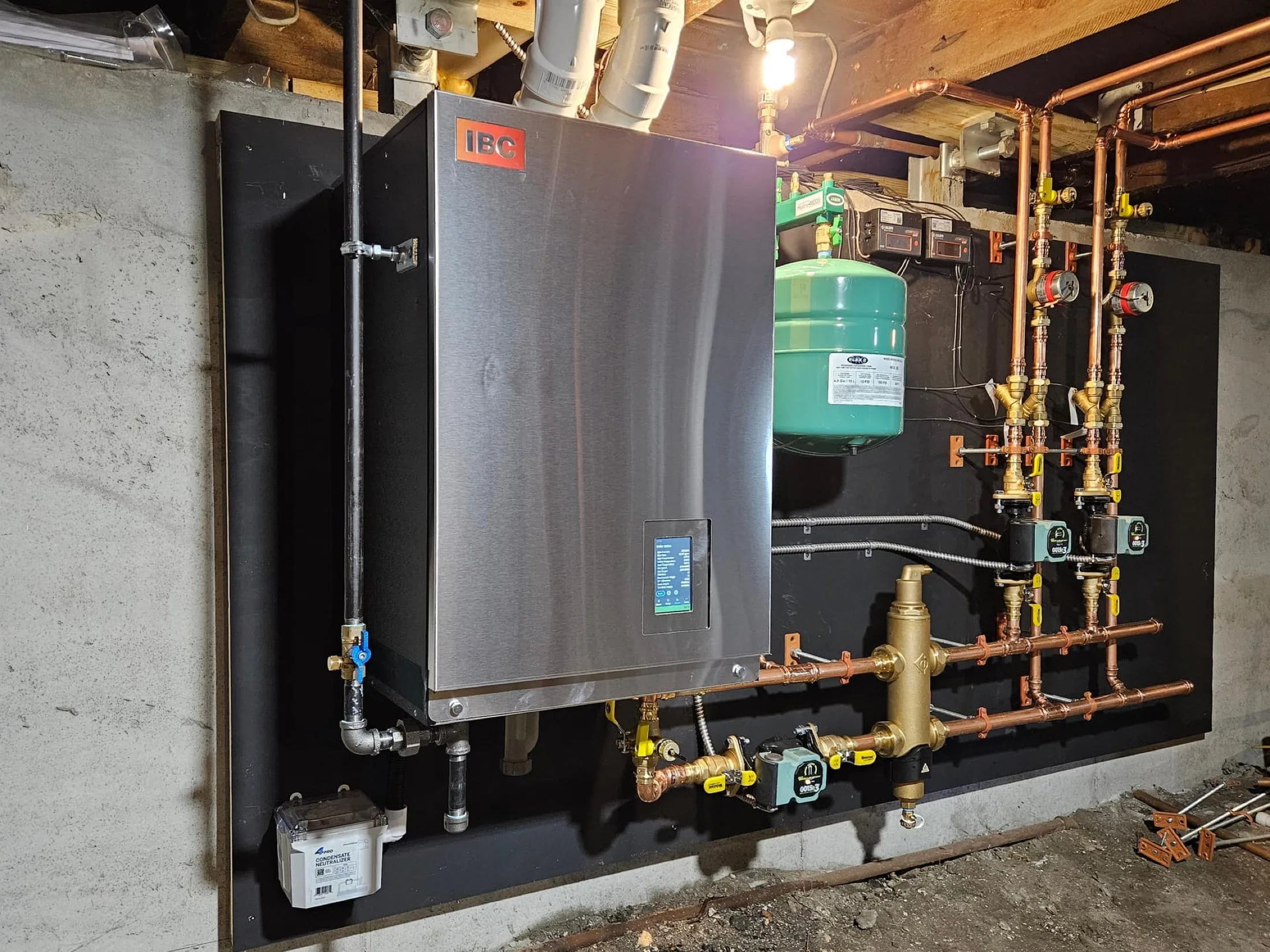 An IBC boiler and copper piping on a basement wall.