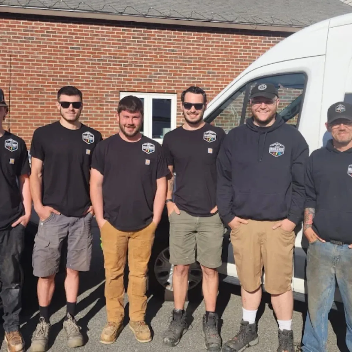 Seven Aces Highlands employees stand between two white service vans outside a brick building.