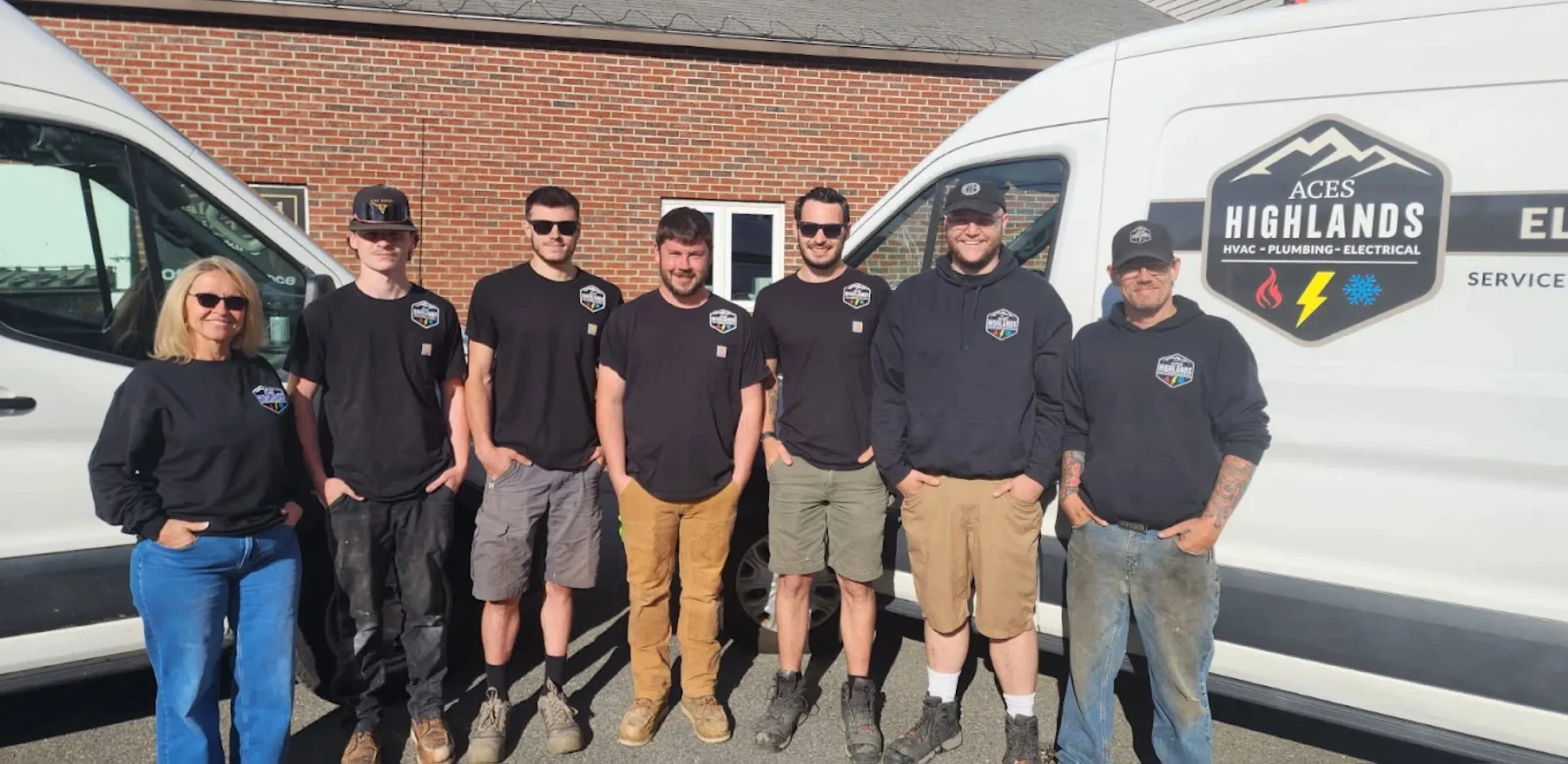 Seven Aces Highlands employees stand between two white service vans outside a brick building.
